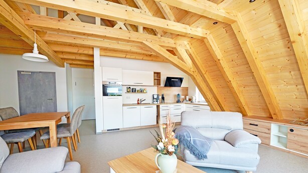 Un loft moderno con vigas de madera a la vista, un comedor, una sala de estar con sofá y mesa de centro, y una kitchenette.