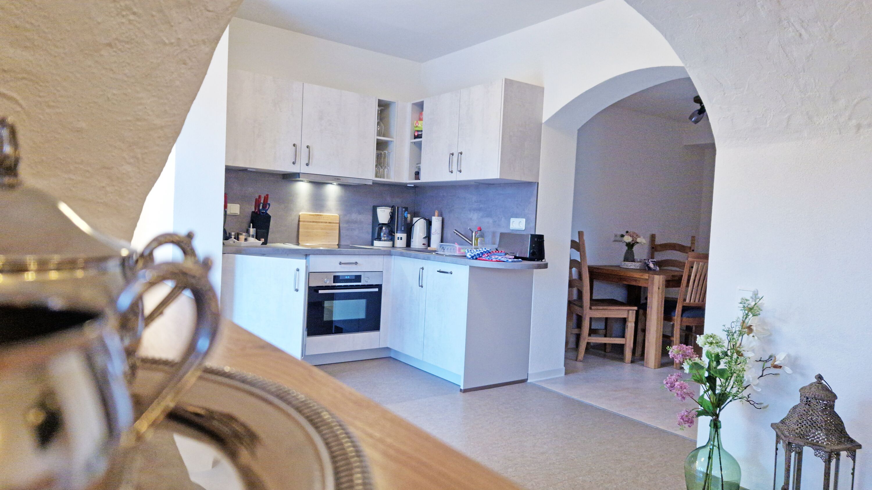 A modern kitchen with white cabinets, a coffee maker, and a dining area with wooden chairs.