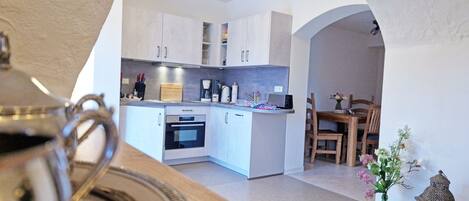 A modern kitchen with white cabinets, a coffee maker, and a dining area with wooden chairs.