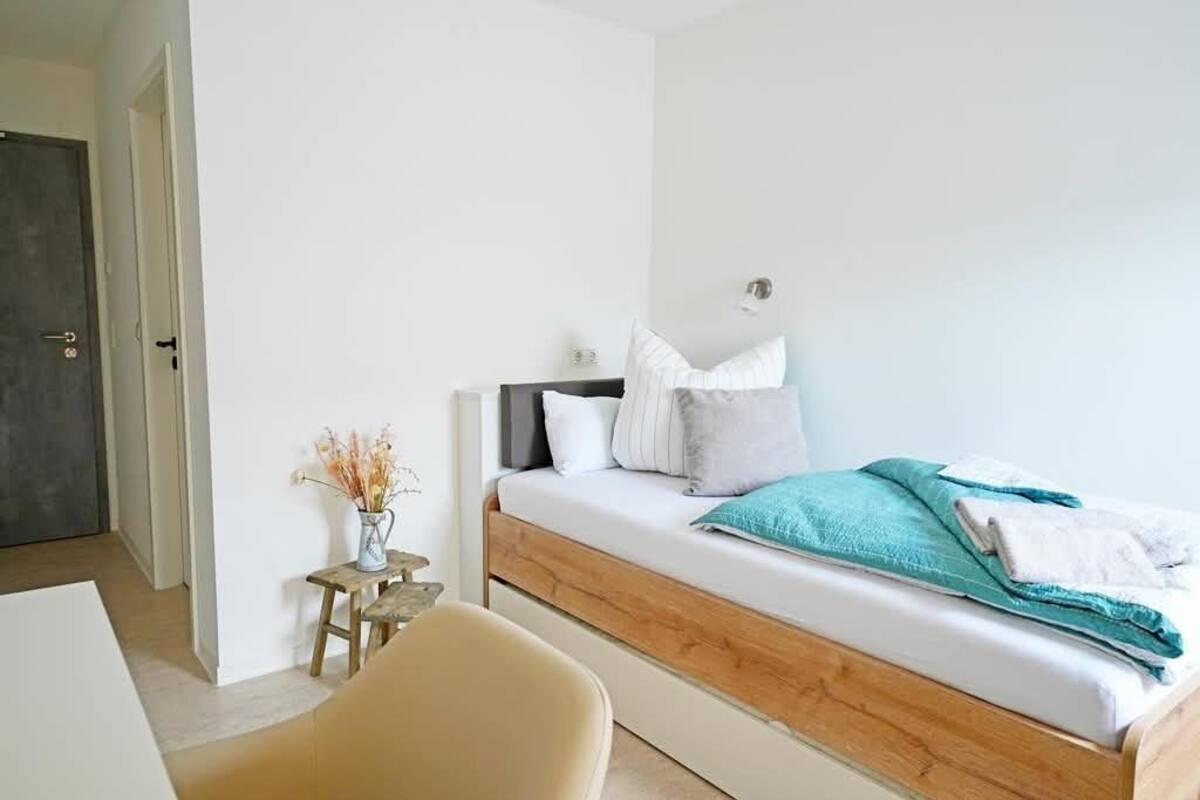 Un dormitorio con una cama, una mesita con un florero y una puerta.