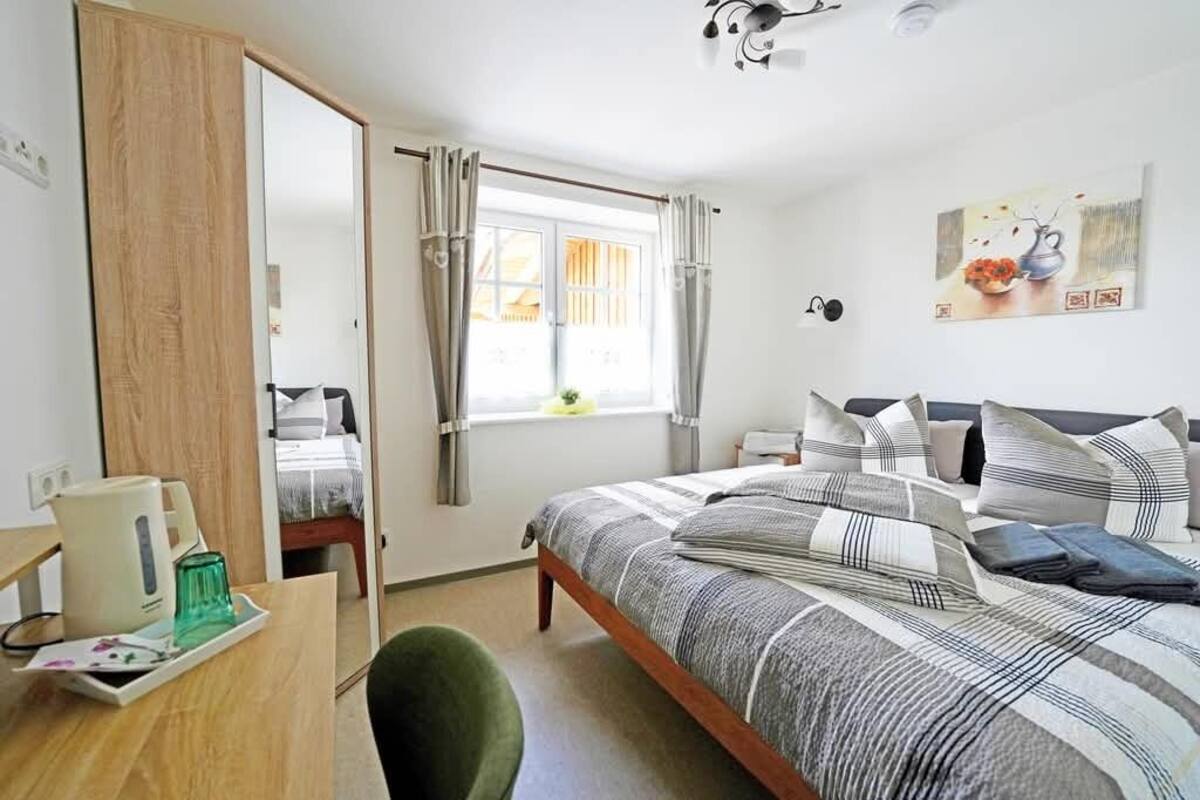 Un dormitorio con cama, escritorio, silla, ventana con cortinas y un cuadro en la pared.
