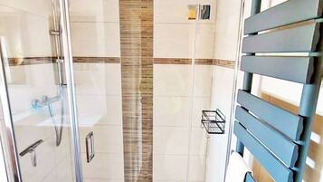 A modern bathroom with a glass shower enclosure, a wooden ceiling, and a tiled floor.