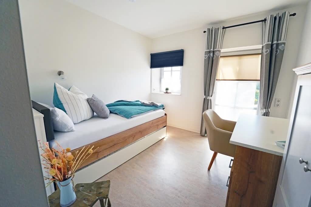 A bedroom with a bed, a window with curtains, a desk, and a chair.