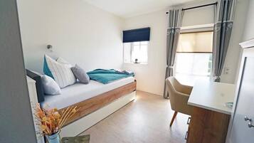 A bedroom with a bed, a window with curtains, a desk, and a chair.