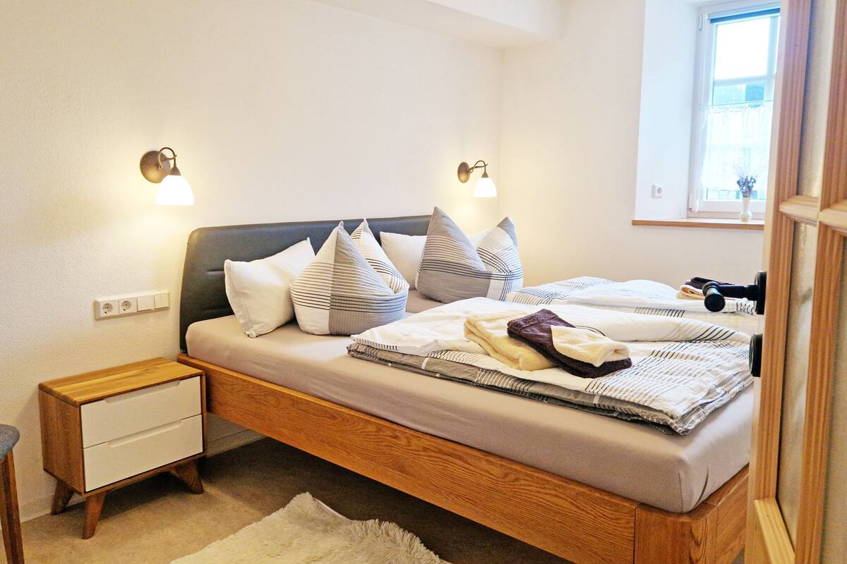 Un dormitorio con cama, mesitas de noche, una silla y un ventanal.