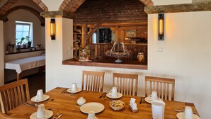 Un comedor con mesas y sillas de madera, y un horno de ladrillo al fondo.