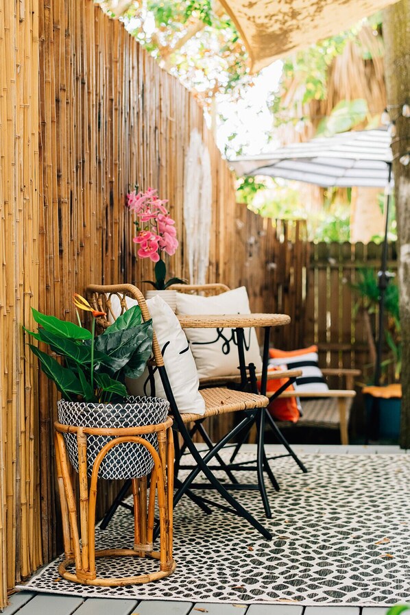 A wicker chair with a potted plant, a cushioned bench, and a patterned floor. - The Twisted Tulip A Curious and Intimate Garden Studio (St. Petersburg)