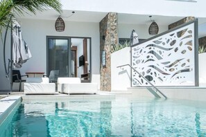 A modern pool area with white lounge chairs, a stone pillar, and a decorative white partition.