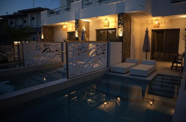 A modern poolside area with a glass enclosure, outdoor seating, and ambient lighting.