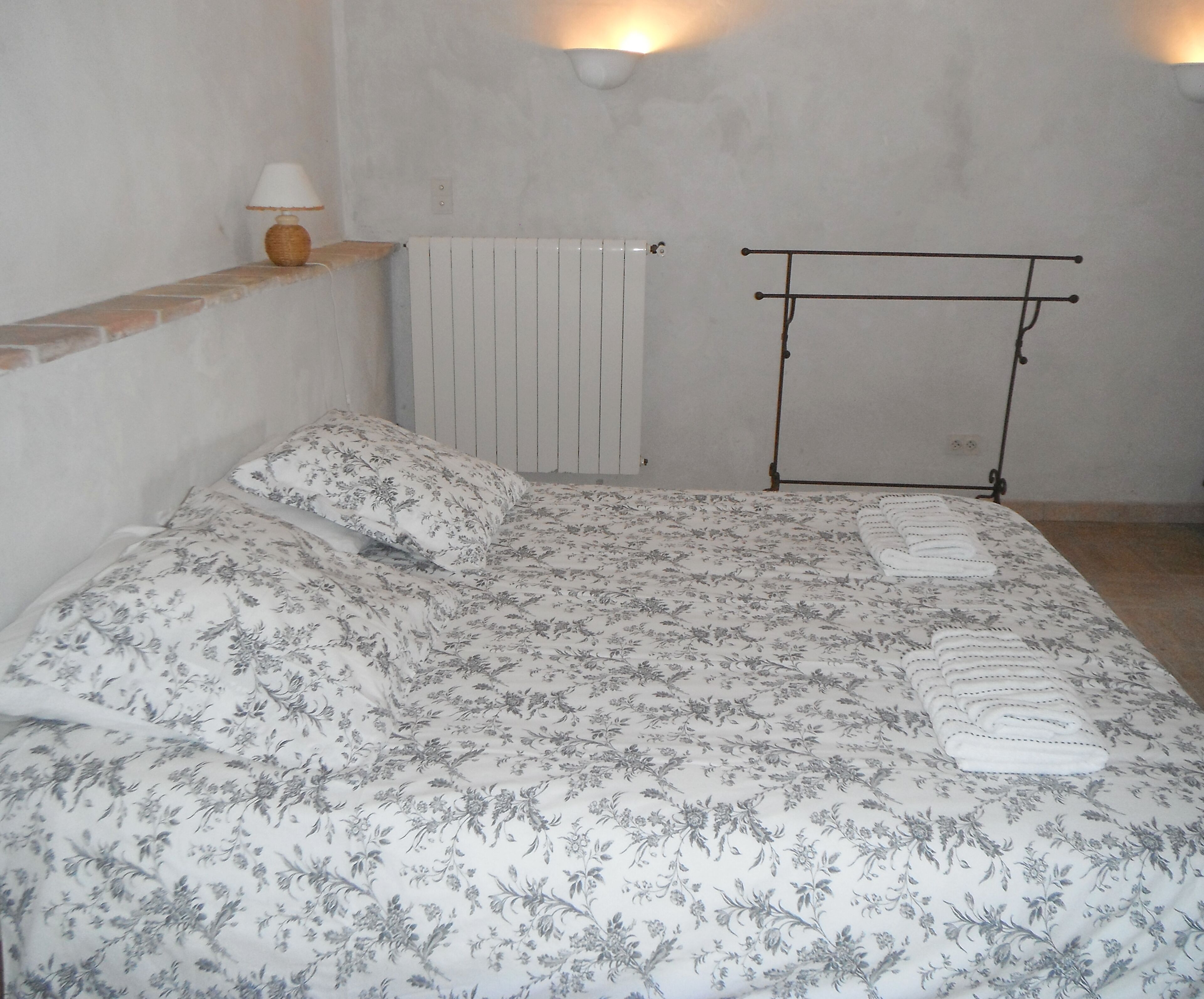 A bedroom with a bed, a radiator, a wall-mounted lamp, and a towel rack.