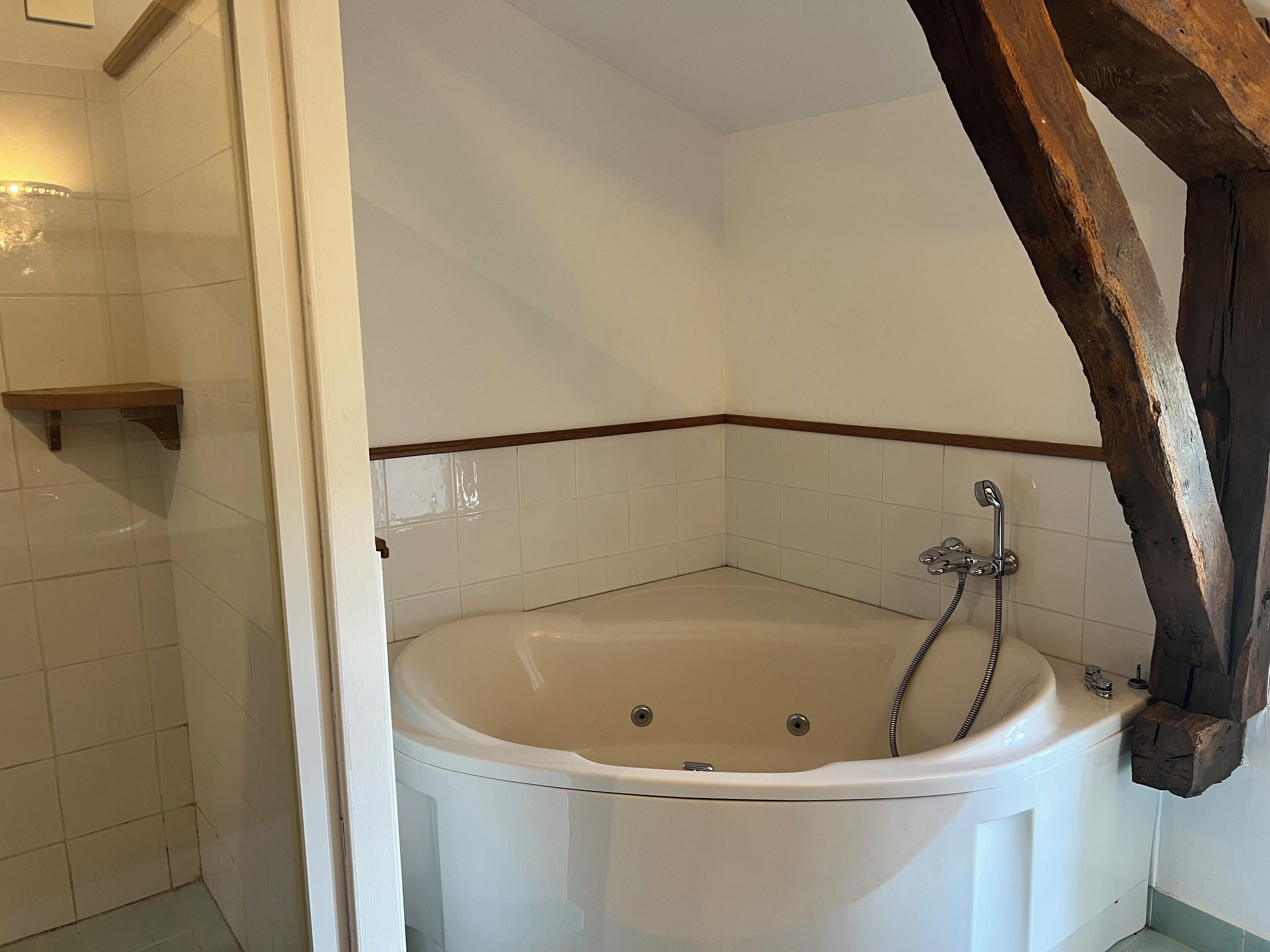 A corner bathroom with a bathtub, a wooden beam, and a small shelf.