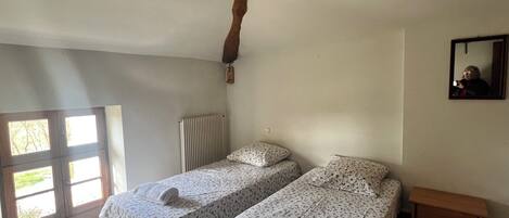 A bedroom with two single beds, a wooden bench, a radiator, and a mirror on the wall.