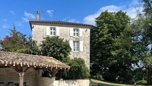 A swimming pool with lounge chairs, a stone building with a tiled roof, and lush greenery in the background. - Private swimming pool - Charming Quercy stone house (Roquecor)