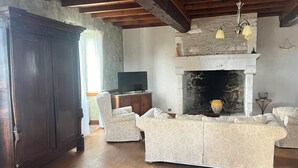 A living room with a fireplace, wooden beams, a television, and patterned furniture. - Private swimming pool - Charming Quercy stone house (Roquecor)
