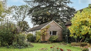 A small wooden house with a sloped roof, surrounded by a well-maintained garden with various plants and flowers. - Brooklands Farm Cottage (Biggleswade)