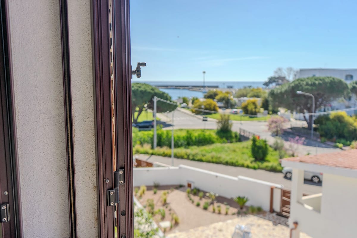 A view from a window overlooking a residential area with a street, greenery, and a body of water in the distance.