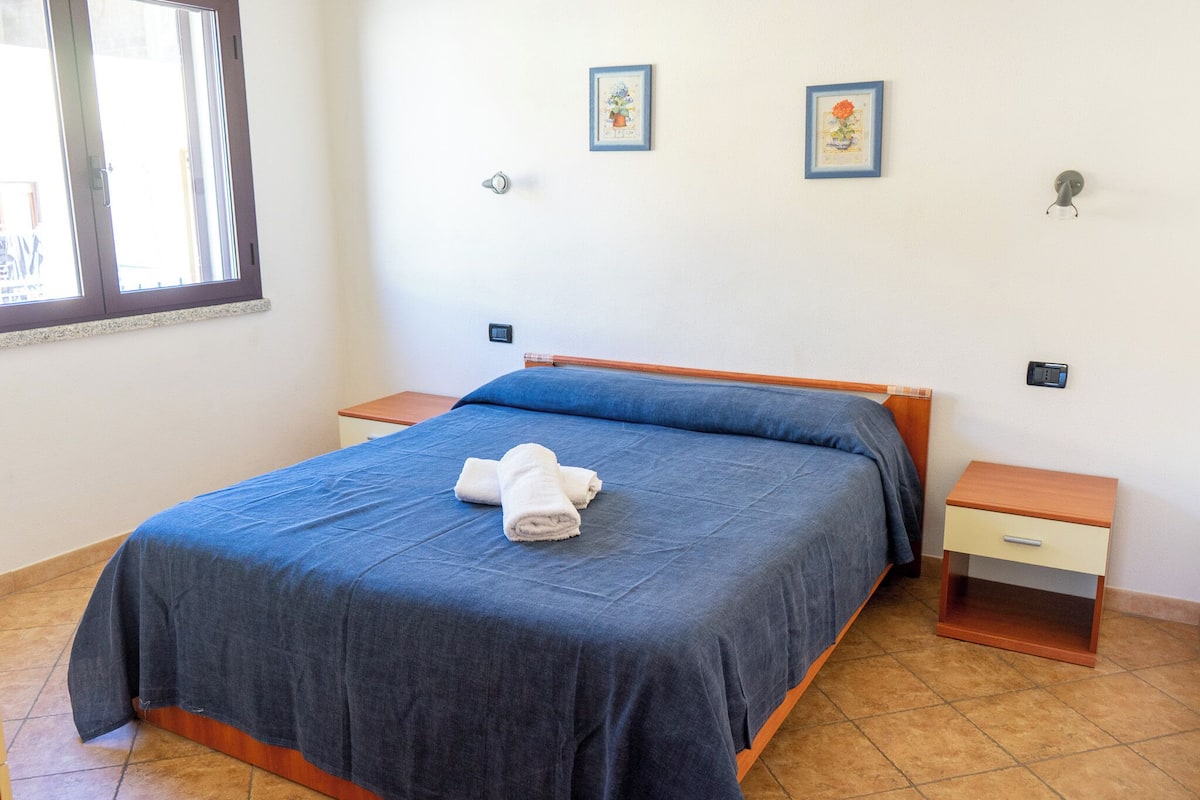 A neatly made bed with a blue bedspread and white towels, a wooden headboard, and a small bedside table with a drawer.