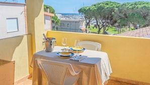 A balcony with a table set for two, a metal bucket, and a clear view of the sea and trees in the background. - Porto Apartments - La Caletta (Siniscola)