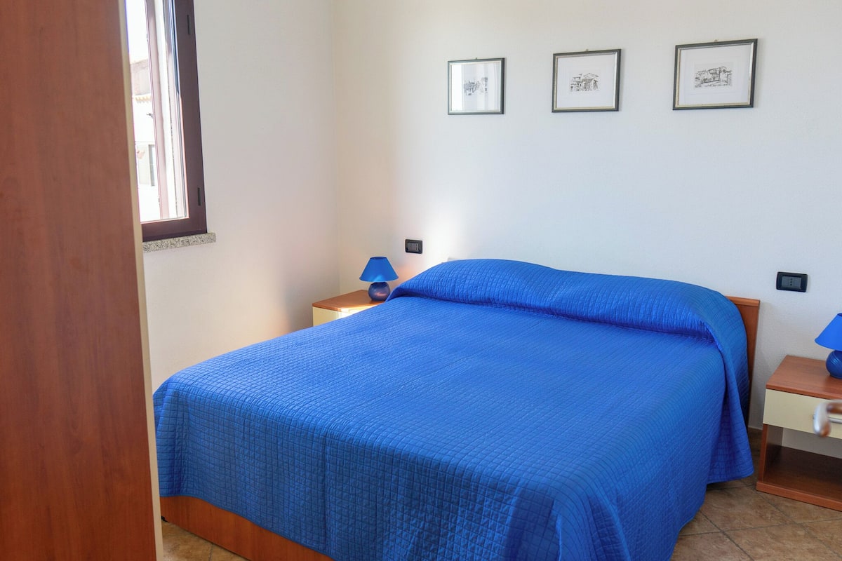 A bedroom with a bed, a nightstand, a lamp, and framed pictures on the wall.