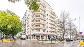 A multi-story building with balconies, a parking area, and a street with cars and trees. - GuestReady - A comfortable stay in Lisbon (Lisbon)
