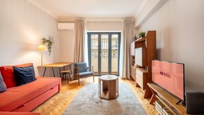 A modern living room with a sofa, a coffee table, a TV, and a balcony with curtains. - GuestReady - A comfortable stay in Lisbon (Lisbon)