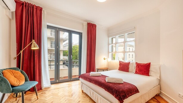 A hotel room with a bed, a chair, a nightstand, and a window with a view of buildings. - GuestReady - A comfortable stay in Lisbon (Lisbon)