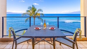 A balcony with a table set for two, overlooking a beach with the ocean and a palm tree.