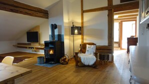 A cozy living room with a wood-burning stove, a comfortable sofa, a television, and a dining area.