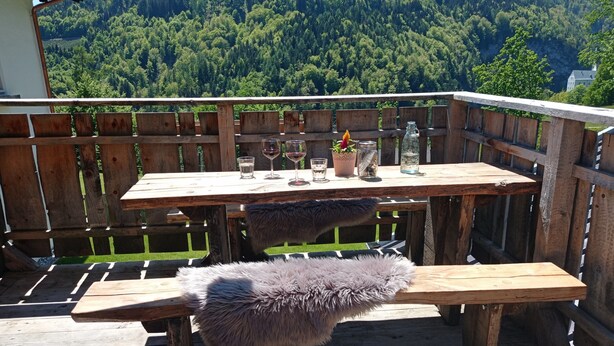 A wooden deck with a table and bench, overlooking a forested mountain.