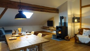 A cozy loft-style living space with a wooden dining table, a fireplace, a television, and a comfortable seating area.