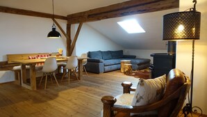 A cozy loft-style room with a dining area, a sofa, and a large window.