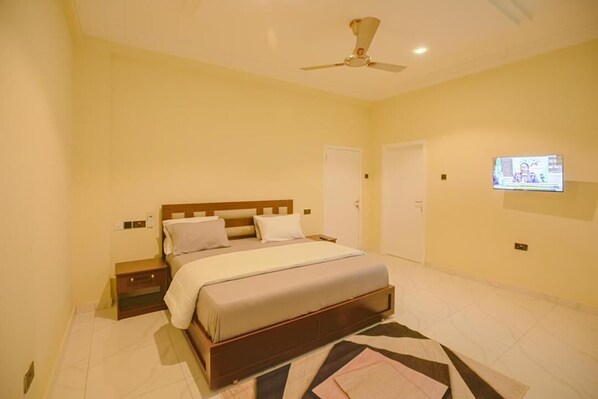 A bedroom with a bed, bedside tables, a ceiling fan, a TV mounted on the wall, and a door.