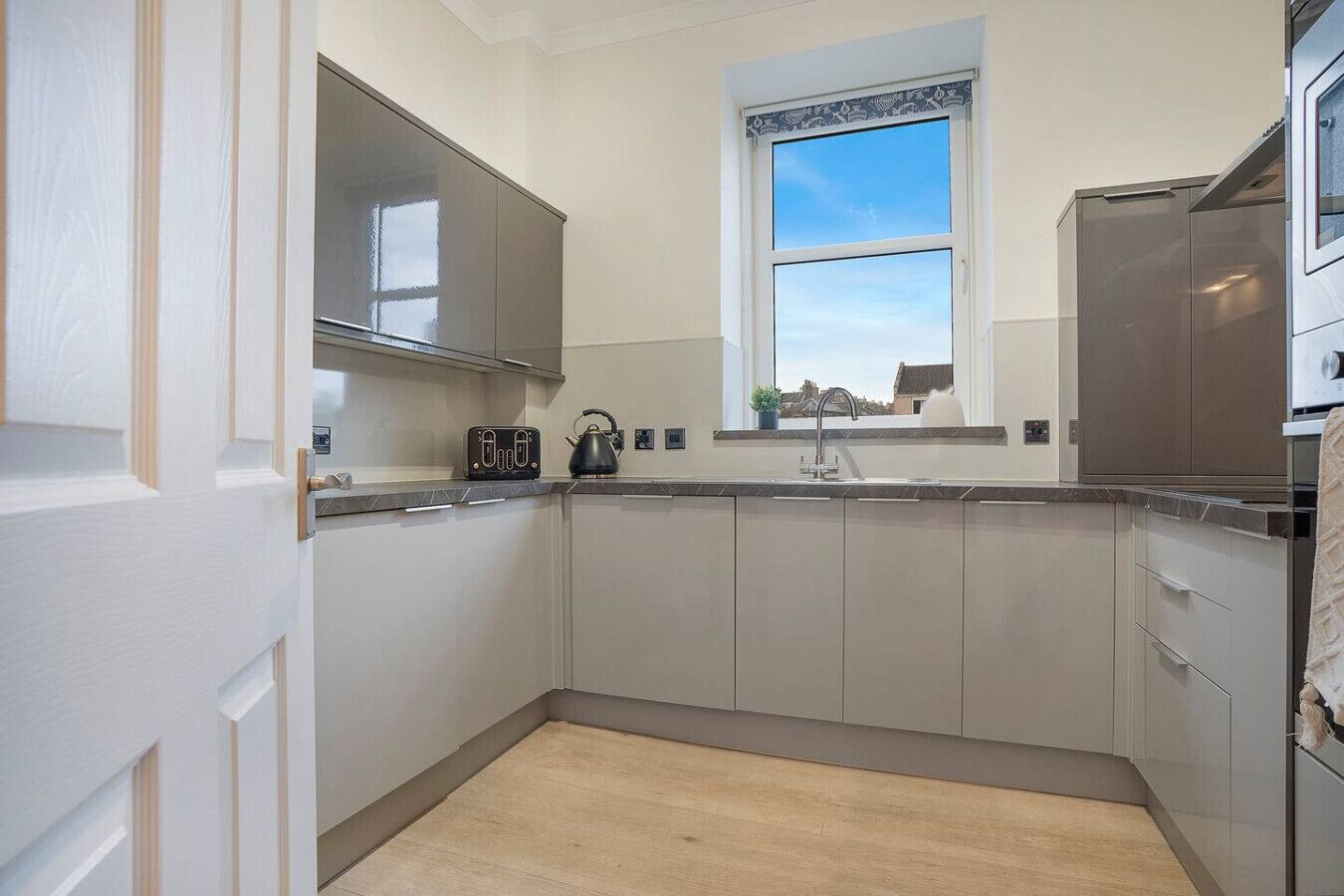 A modern kitchen with white cabinetry, a built-in oven, and a window above the sink.