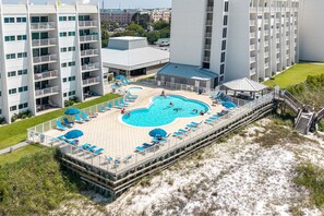 A swimming pool with a deck, surrounded by lounge chairs and umbrellas, adjacent to a building with multiple balconies.