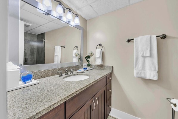 A bathroom with a granite countertop, a white sink, a large mirror with lights, and a towel rack.
