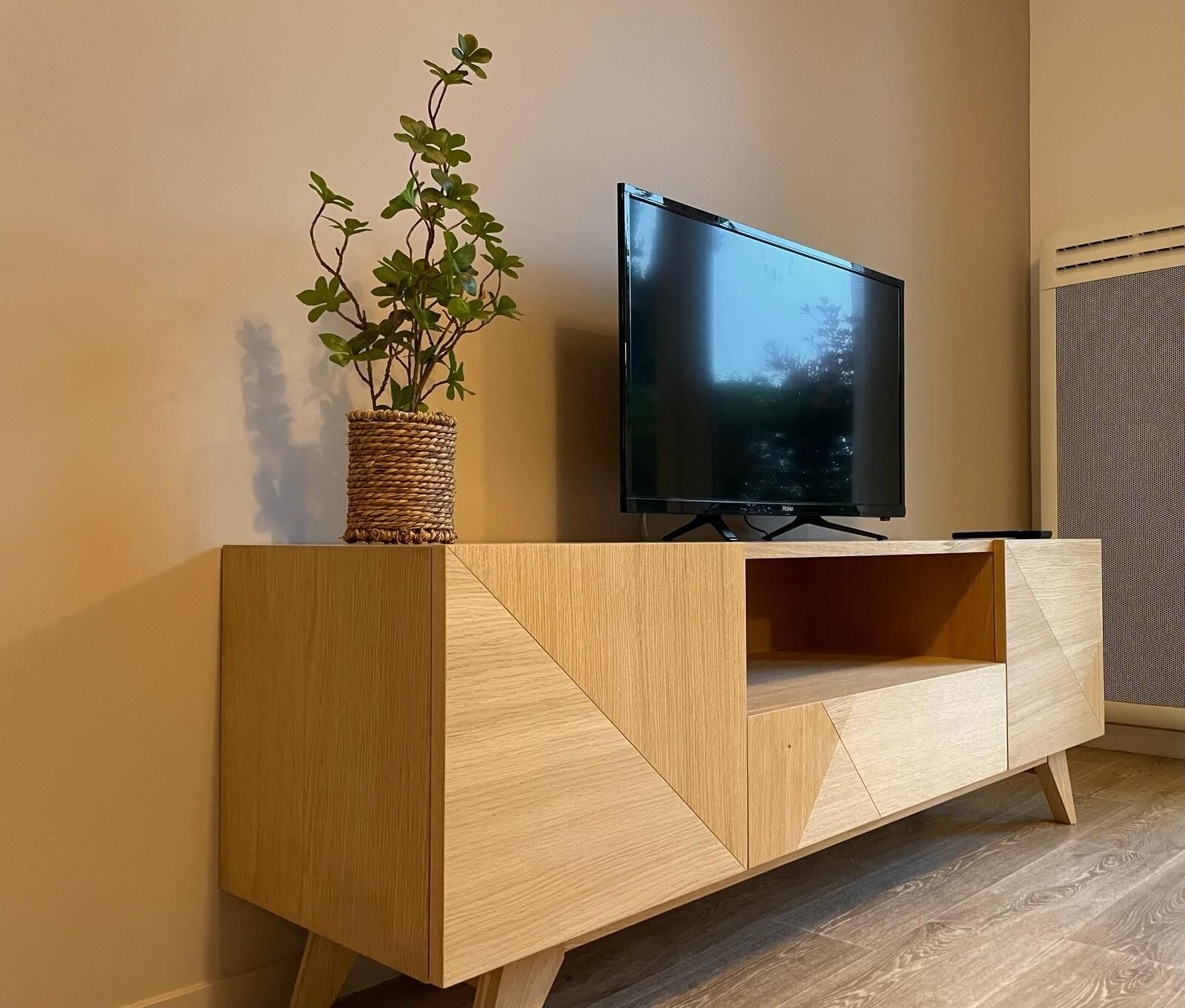 Et moderne tv-skab i træ med et fladskærms-tv og en plantekasse i fletværk.
