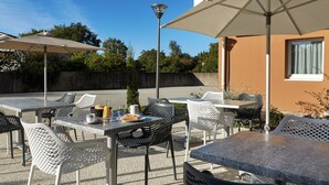 An outdoor patio with tables and chairs, umbrellas, and a street lamp. - Zenao Appart'hôtels Challans (Challans)