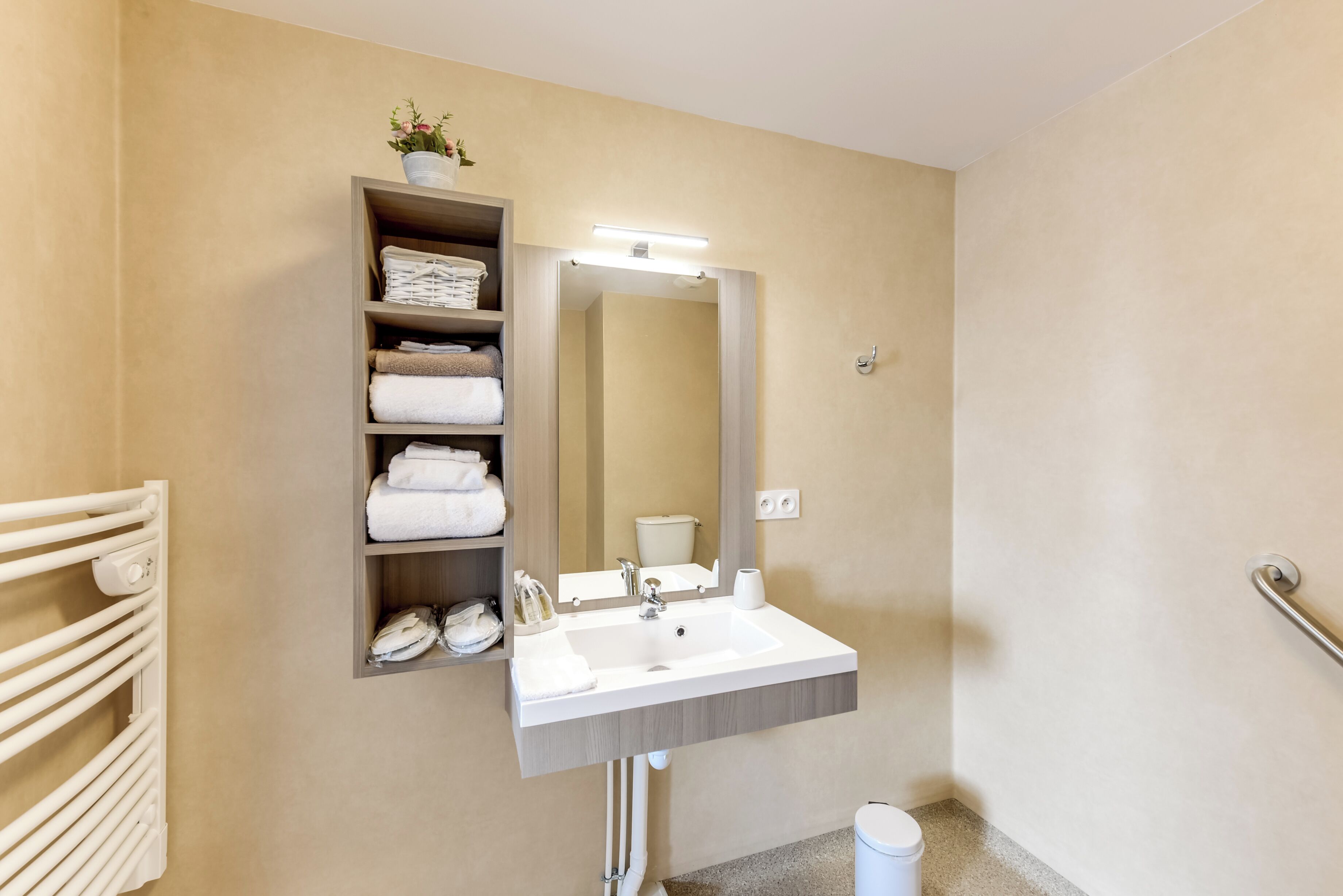 A bathroom with a white sink, a mirror, a towel rack, and a shelf with folded towels.