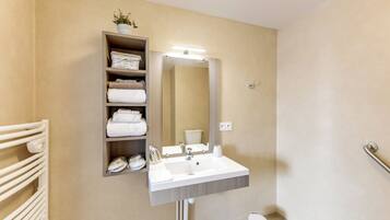 A bathroom with a white sink, a mirror, a towel rack, and a shelf with folded towels.
