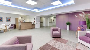 A modern lobby with a reception desk, seating area, and a purple accent wall. - Zenao Appart'hôtels Challans (Challans)