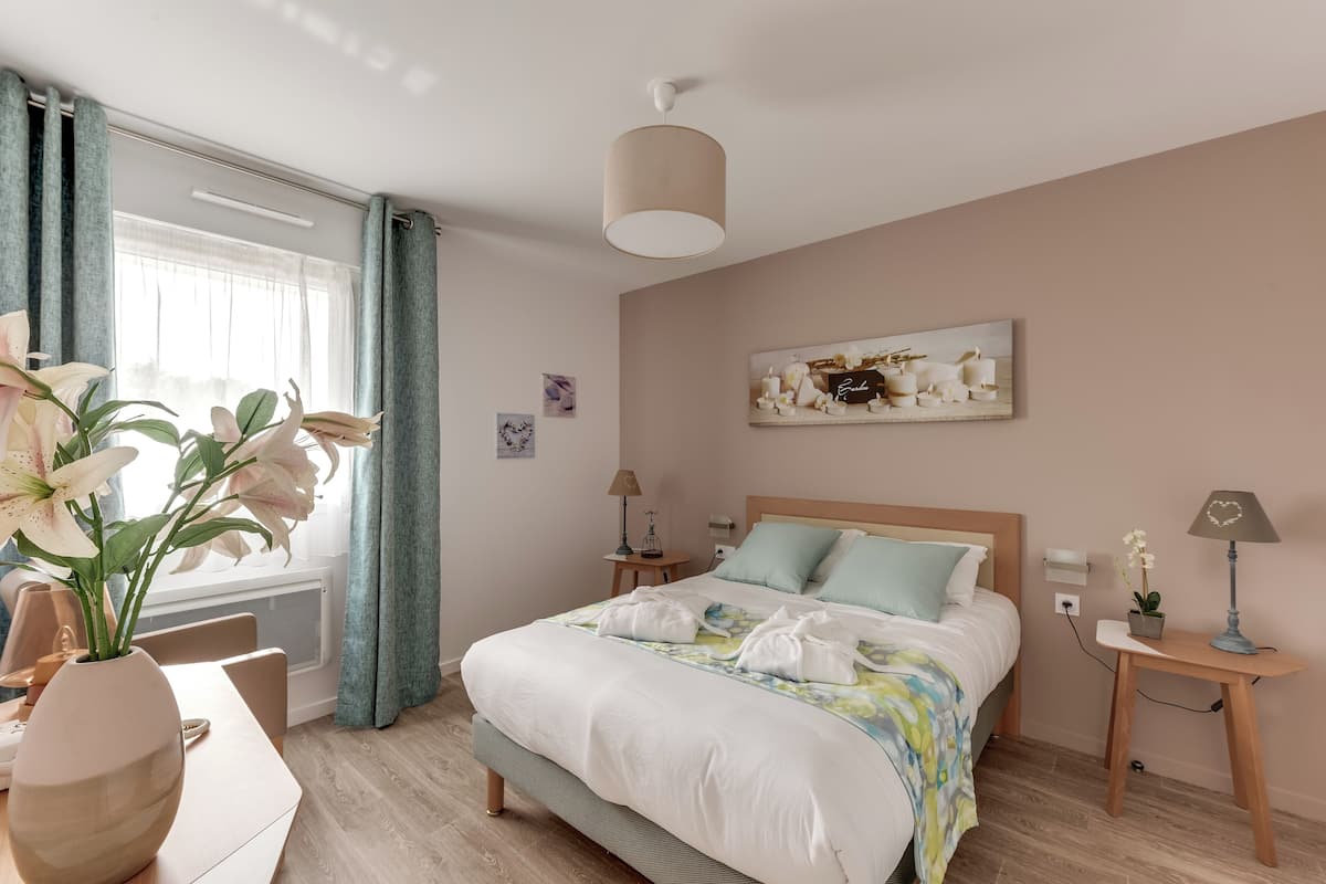 Un dormitorio ordenado con cama, mesitas de noche, lámpara y un jarrón de flores.