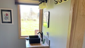 A compact kitchen with a window, wooden counter, and a metal rack. - Rifle River Lodge, Rifle River Lodge LLC (Rose City)