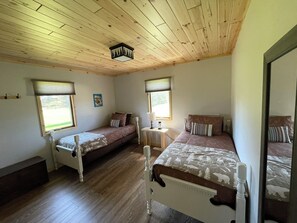 Um quarto com duas camas de solteiro, teto de madeira e janela com vista para o verde.
