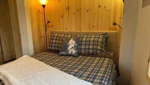 A bedroom with a plaid bedspread, a white throw blanket, and two lamps on either side of the bed. - Rifle River Lodge, Rifle River Lodge LLC (Rose City)