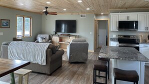 A spacious living area with a wooden ceiling, a flat-screen TV, and a kitchen with modern appliances. - Rifle River Lodge, Rifle River Lodge LLC (Rose City)