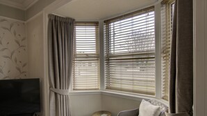 A corner room with a television, a small round table, a chair, and a window with blinds. - The Clachan Wick in Wick (Wick)