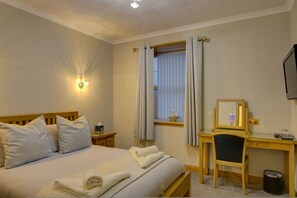 Habitación de hotel con cama, escritorio, silla, ventana con cortinas, televisor montado en la pared y lámpara mural.