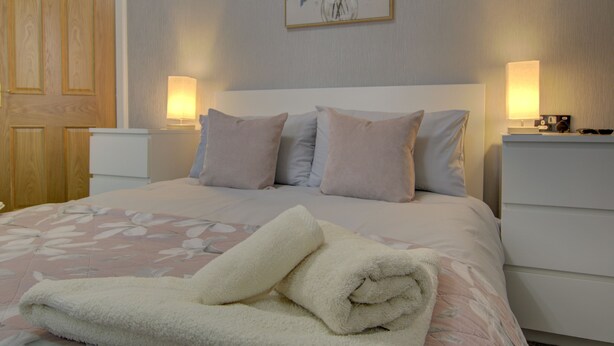 A neatly made bed with a floral bedspread, two bedside lamps, and a wooden door. - The Clachan Wick in Wick (Wick)