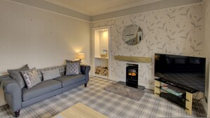 A living room with a sofa, a fireplace, a television, and patterned wallpaper. - The Clachan Wick in Wick (Wick)