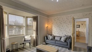 A living room with a plaid carpet, a grey sofa with cushions, a wooden coffee table, a chair, and a lamp. - The Clachan Wick in Wick (Wick)